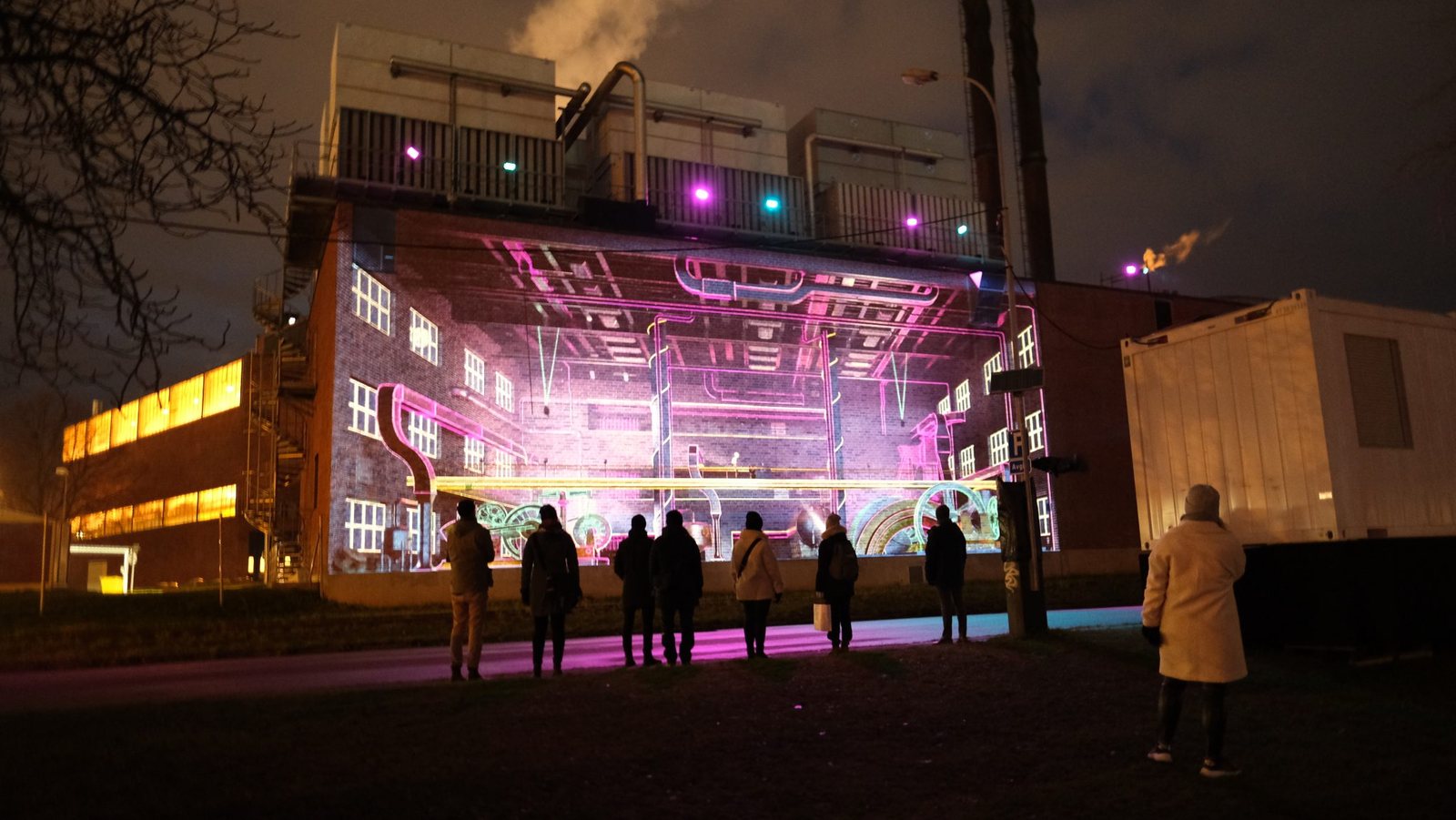 Large-scale projection mapping on an industrial building at night, with an audience watching