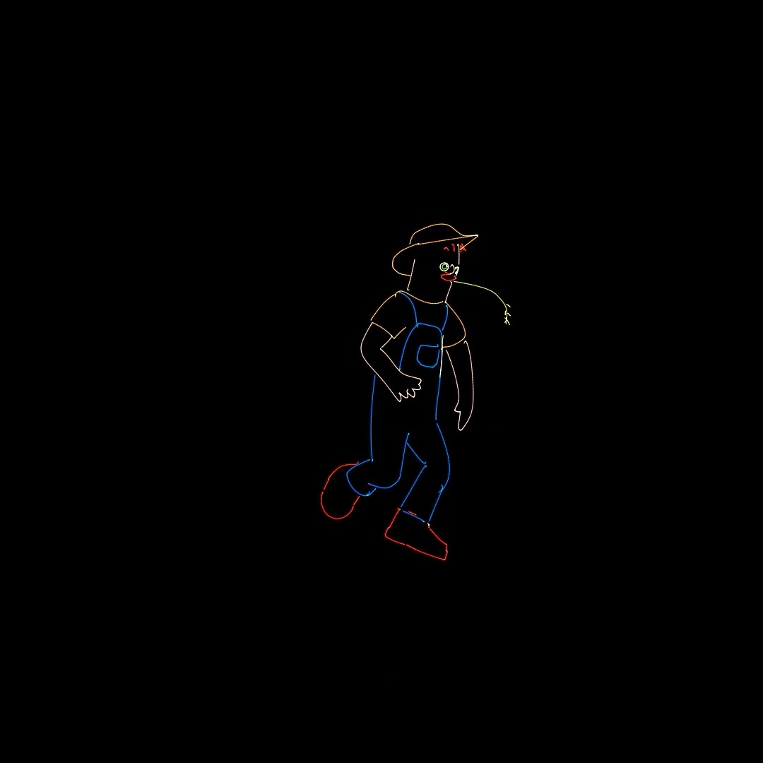 A farmer in a hat and dungarees walking with a piece of straw